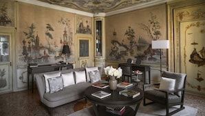 Een kamer met een grote bank, een ronde salontafel met boeken, een vaas met bloemen en een lamp.