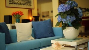 Ett vardagsrum med en blå soffa, ett vitt bord och en vas med blå blommor.