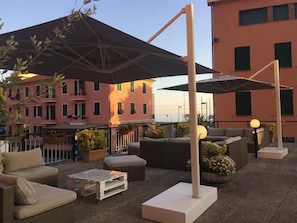 An outdoor seating area with wicker furniture, a white table, and umbrellas. - Hotel Doria Lavagna (Lavagna)