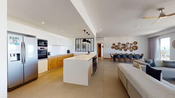 A modern kitchen with a central island, a dining area with a round table, and a living room with a sofa and a ceiling fan.