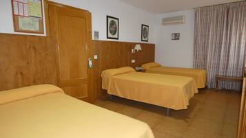 Habitación de hotel con tres camas individuales, un armario de madera, aire acondicionado instalado en la pared y una cortina.