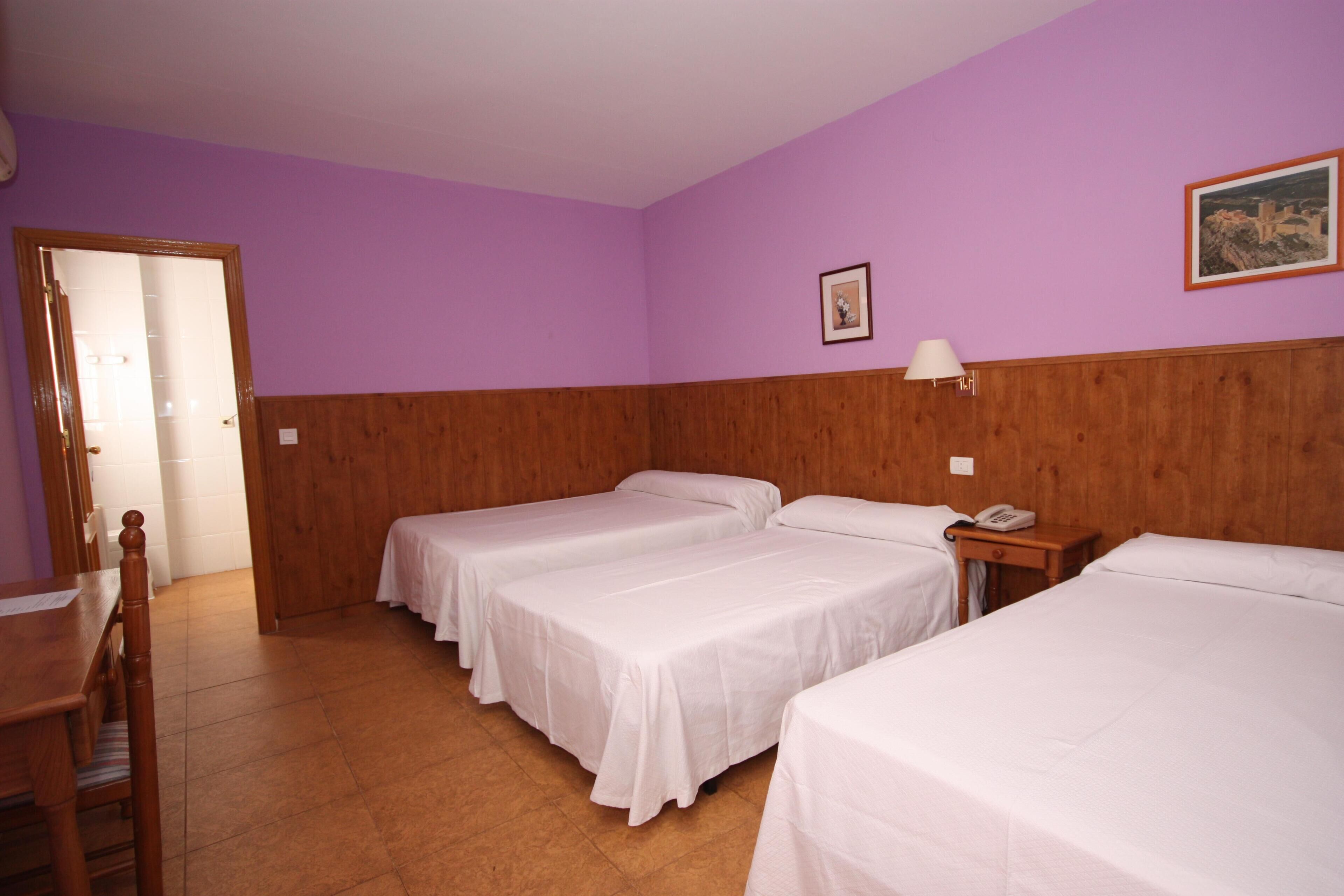 Una habitación con tres camas individuales, cabeceros de madera, una mesa de madera y una silla.