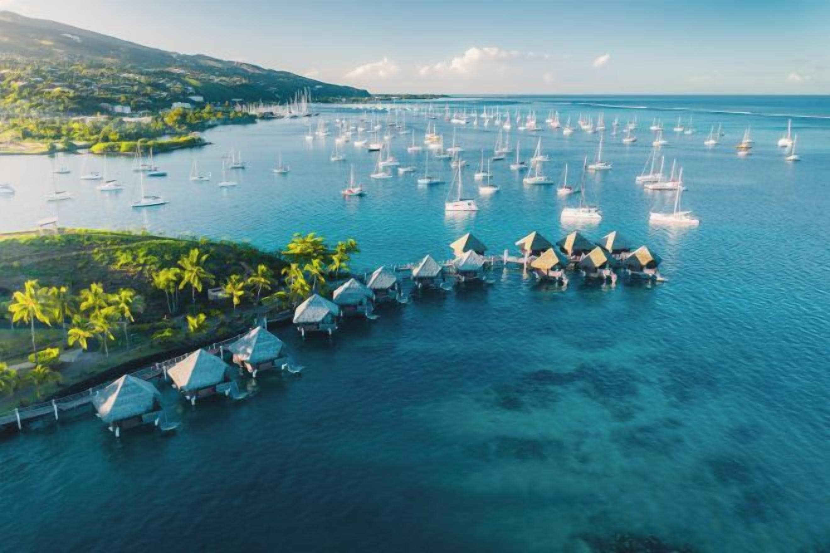 An aerial view of a coastal area with numerous boats docked near overwater bungalows.
