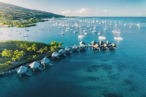 An aerial view of a coastal area with numerous boats docked near overwater bungalows.