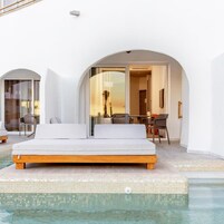 Un área de piscina moderna al aire libre, con un banco y un sofá de madera, una puerta de vidrio que da a un comedor y una vista despejada de la piscina.