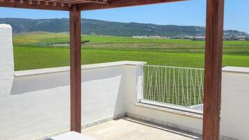 A balcony with a pergola, a view of green fields, and a distant mountain range.