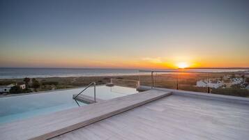 A rooftop infinity pool with a view of the sunset over the ocean.