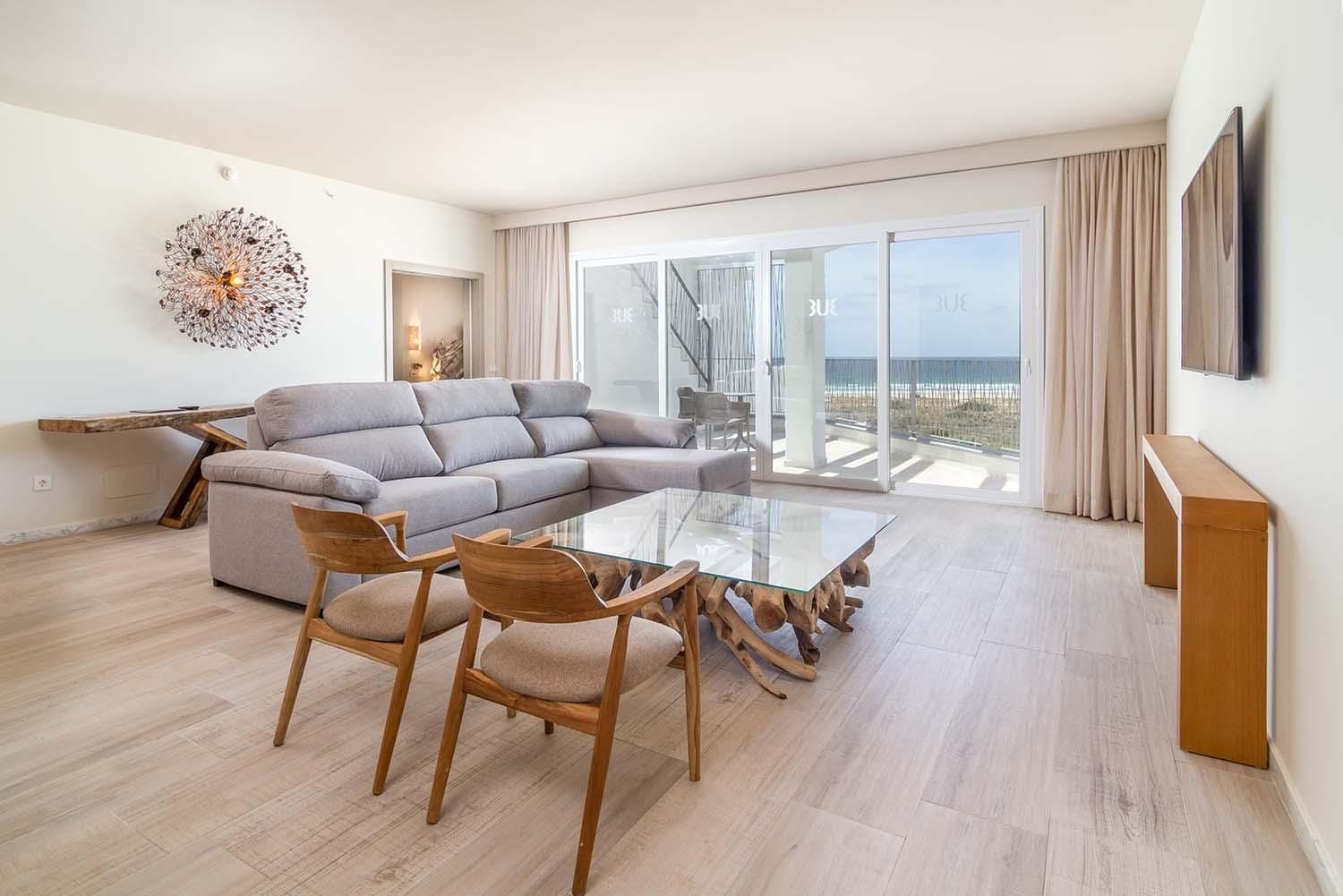 A modern living room with a sectional sofa, a glass-top dining table, and wooden chairs.