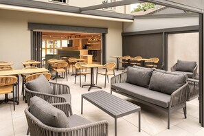 An outdoor seating area with wicker furniture, a sofa, and a bar visible through an open doorway. - Sure Hotel by Best Western Tours Sud (Chambray-les-Tours)