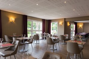 Ein Restaurant mit mehreren Tischen und Stühlen, großen Fenstern und Wandleuchten.