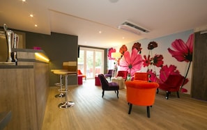 Un intérieur moderne avec un bar, des espaces pour s’asseoir et une fresque murale à motifs floraux.