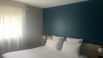 Una habitación de hotel con cama, cortinas y una pared azul.