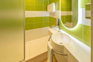 Une salle de bain avec un lavabo blanc, des carreaux verts, un miroir et un porte-serviettes.