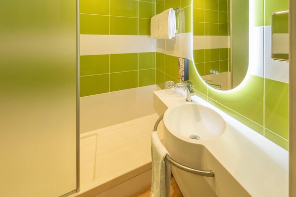 A bathroom with a white sink, green tiles, a mirror, and a towel rack. - Sure Hotel by Best Western Tours Sud (Chambray-les-Tours)