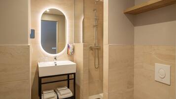 Un baño moderno con lavamanos, espejo, toallero, ducha y estante de madera.