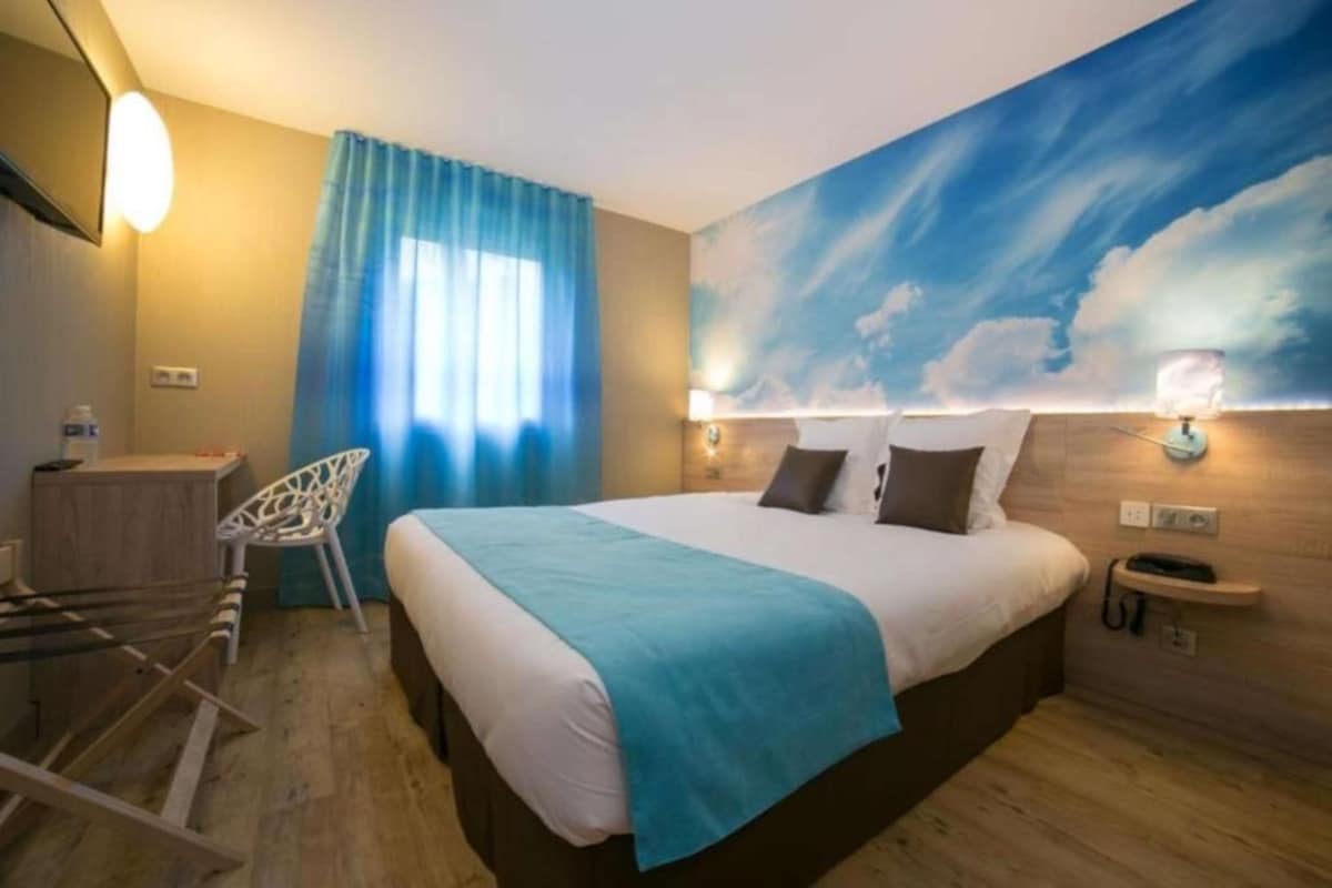 Ein Hotelzimmer mit Bett, Stuhl, Schreibtisch und Wandgemälde.