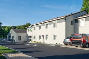 A modern building with a parking area, a van, and a car parked outside.