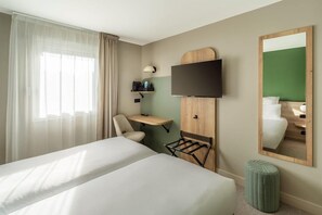 Une chambre d’hôtel avec deux lits, un bureau, une chaise, une télévision, un miroir et un petit pouf.