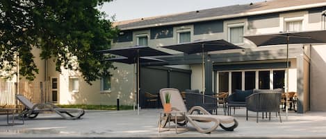 A poolside area with lounge chairs, umbrellas, and a building in the background.