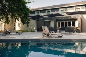 Zona de piscina con sillones reclinables, sombrillas y un edificio al fondo.