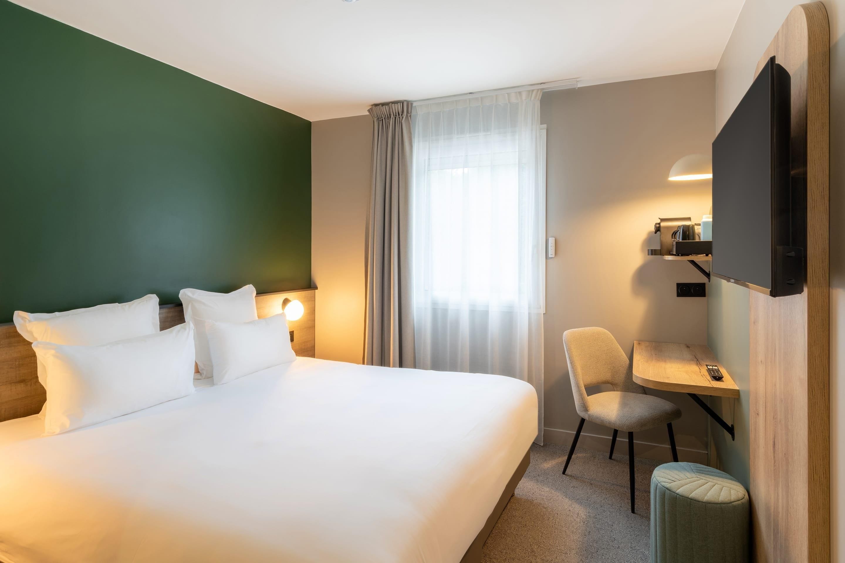 A hotel room with a large bed, a desk, a chair, and a television.