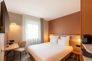 Habitación de hotel con cama, escritorio, silla, una mesita pequeña y un dispositivo instalado en la pared.