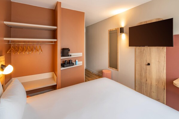 A hotel room with a bed, a wardrobe, a mirror, a television, and a shelf with toiletries. - Sure Hotel by Best Western Tours Sud (Chambray-les-Tours)
