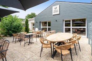 An outdoor patio with round tables and wicker chairs, a sign reading 'VIEILLES BRANCHES,' and a building with large windows and a blue exterior. - Sure Hotel by Best Western Tours Sud (Chambray-les-Tours)