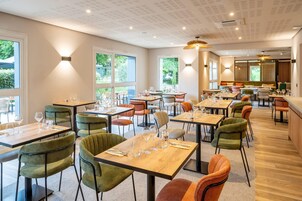 A restaurant with multiple tables and chairs, large windows, and a ceiling with recessed lighting.