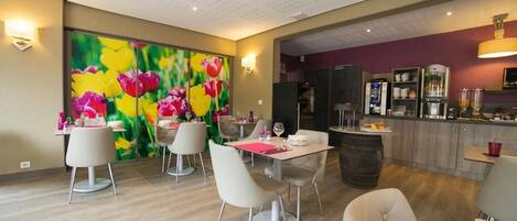 A dining area with a table set for two, a bar area with kitchen appliances, and a vibrant floral mural on the wall.