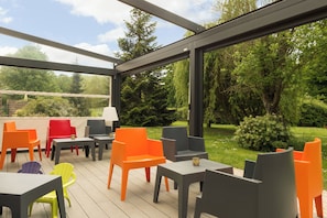 Un espace extérieur abrité, aménagé avec des tables et des chaises, une lampe et offrant une vue sur un jardin.