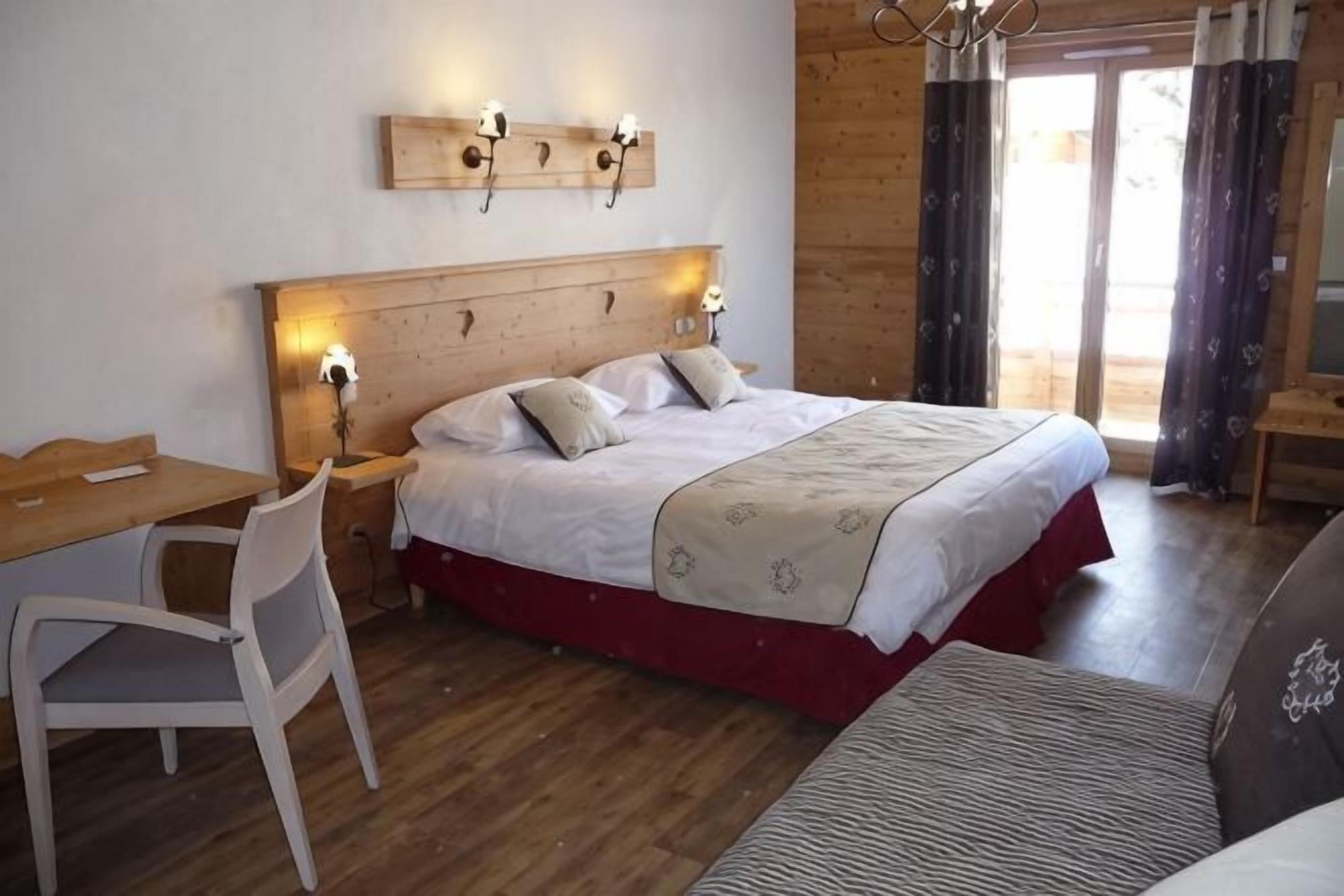 A bedroom with a wooden headboard, a desk, a chair, a bed with a red skirt, and a window with curtains.