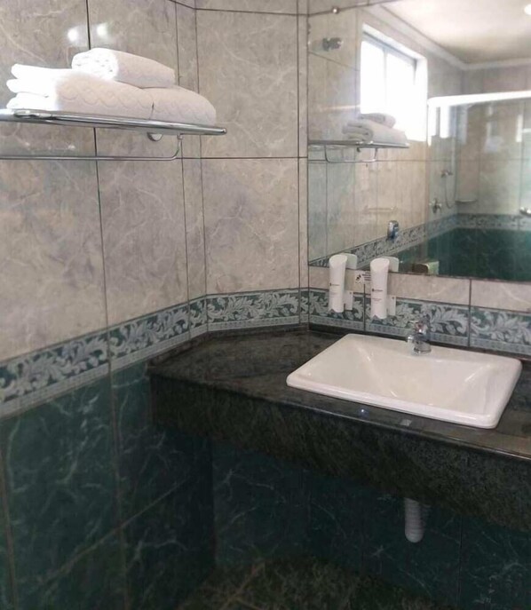A bathroom with a marble wall, a sink, and a mirror. - Astron Suites Sao Jose dos Pinhais (Sao Jose dos Pinhais)
