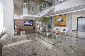 A spacious lobby with a high ceiling, a glass coffee table, a sofa, a TV mounted on the wall, and a staircase leading to an upper level. - Astron Suites Sao Jose dos Pinhais (Sao Jose dos Pinhais)