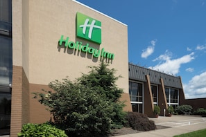 Un hotel Holiday Inn con un logotipo verde destacado, ventanas amplias y un estacionamiento.