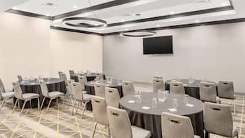 A conference room with round tables, grey chairs, a flat-screen TV, and a patterned carpet.