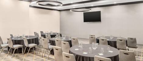 A conference room with round tables, grey chairs, a flat-screen TV, and a patterned carpet.