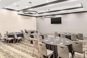 A conference room with round tables, grey chairs, a flat-screen TV, and a patterned carpet. - Holiday Inn & Suites Orlando I-drive Theme Parks (Orlando)