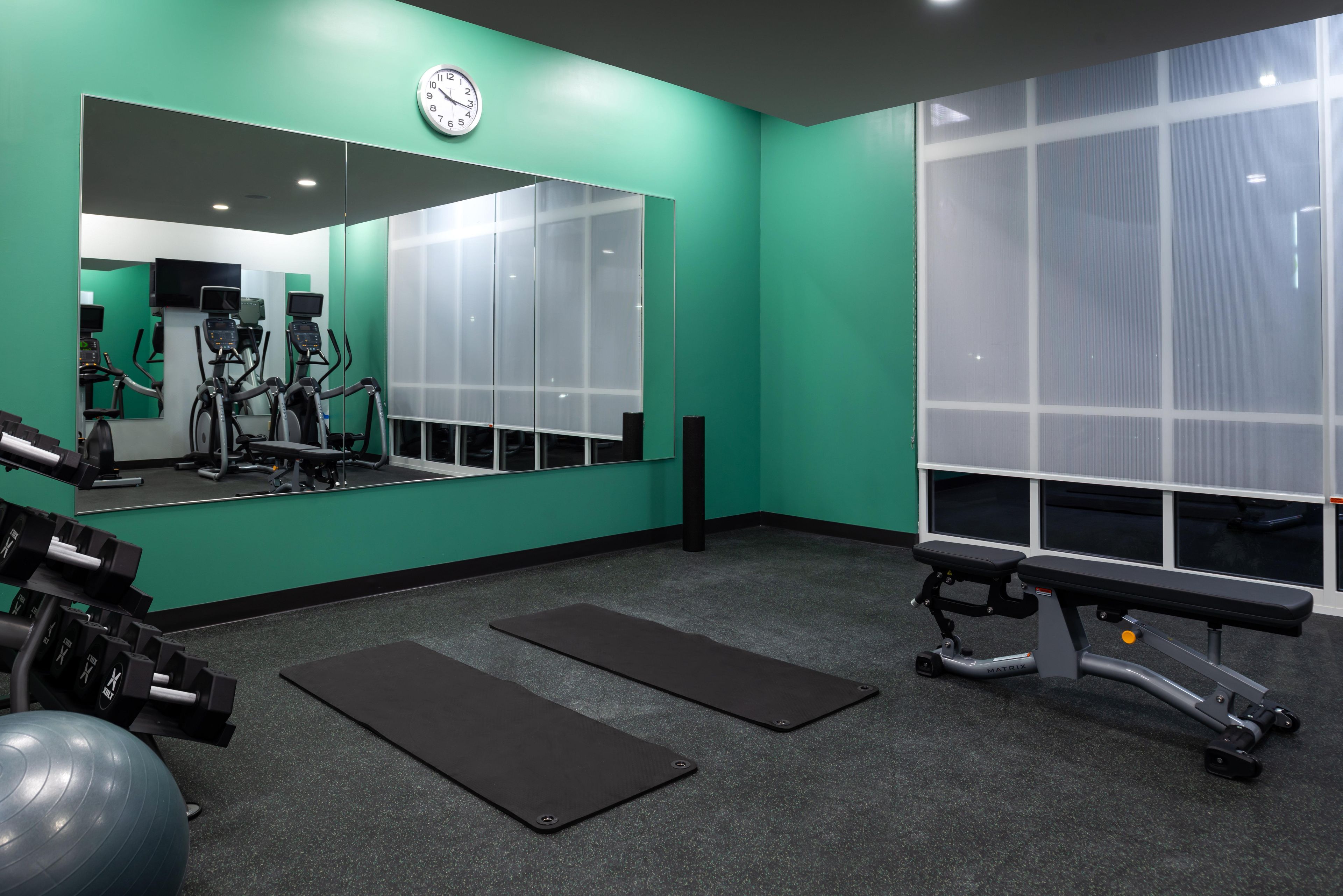 Ein Fitnessstudio mit Trainingsgeräten, einem großen Spiegel und einer Bank.