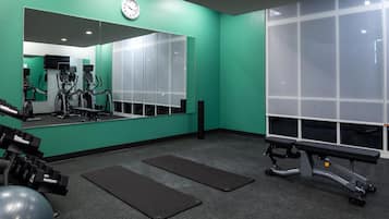 A gym with exercise equipment, a large mirror, and a bench.