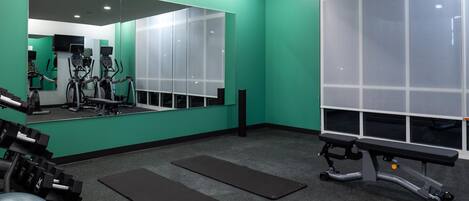 Ein Fitnessstudio mit Trainingsgeräten, einem großen Spiegel und einer Bank.