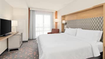 A hotel room with a bed, a TV, a desk with a lamp, a chair, and a patterned carpet.