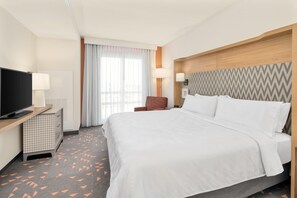 A hotel room with a bed, a TV, a desk with a lamp, a chair, and a patterned carpet. - Holiday Inn & Suites Orlando I-drive Theme Parks (Orlando)