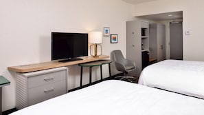 A hotel room with a bed, a desk with a TV, a chair, a small table, and a wardrobe.