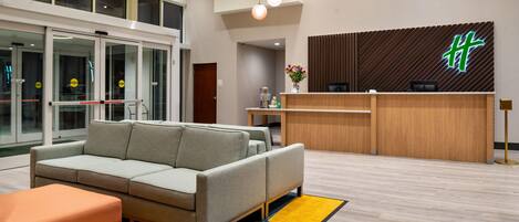 A modern hotel lobby with a reception desk, a sofa, and a glass door entrance.