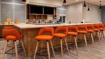 A bar area with orange bar stools, a wooden counter, and pendant lighting.