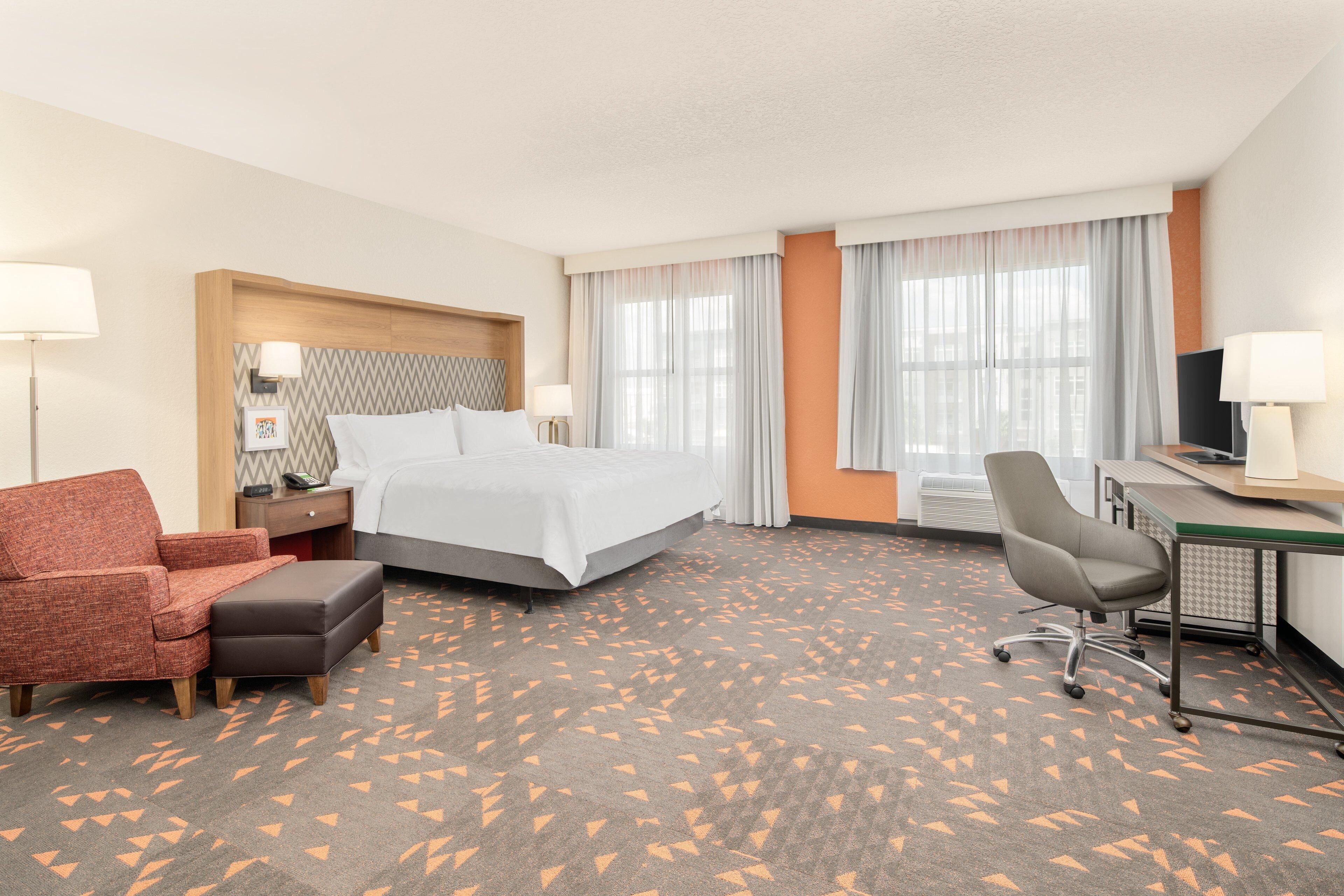 A hotel room with a bed, a desk, a chair, a sofa, and a carpet with a geometric pattern.