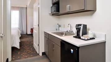 A hotel room with a kitchenette, a bed, a bathroom, and a view of the hallway.