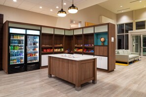 A modern interior with a central wooden table, two beverage dispensers, and a sofa in the background. - Holiday Inn & Suites Orlando I-drive Theme Parks (Orlando)