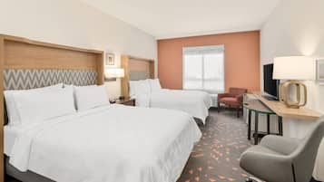 A hotel room with two beds, a desk, a chair, a TV, and a window.